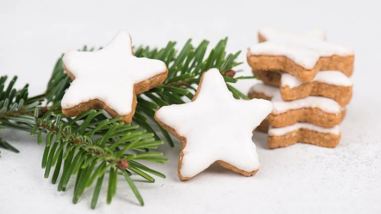 Der Weihnachtsklassiker Zimtsterne lassen sich schnell und einfach aus einer Marzipanrohmasse zubereiten. Sechs Zimtsterne liegen auf einem Tannenzweig. (Foto: Colourbox)