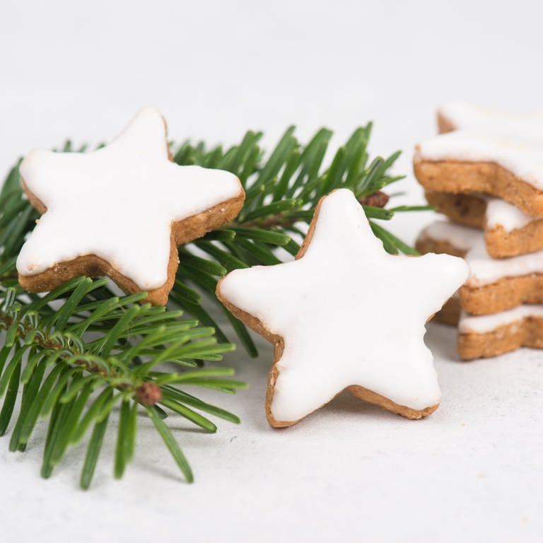Der Weihnachtsklassiker Zimtsterne lassen sich schnell und einfach aus einer Marzipanrohmasse zubereiten. Sechs Zimtsterne liegen auf einem Tannenzweig. (Foto: Colourbox)