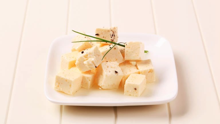 Feta, Hirtenkäse, Käse aus Schafs- oder Ziegenmilch – sie sehen alle ähnlich aus. Aber wo liegt der Unterschied? Fetakäse-Würfel liegen gestapelt auf einem Teller.