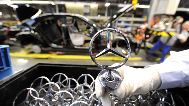 Ein Mitarbeiter hält ein Emblem der Automarke Mercedes-Benz (Foto: dpa Bildfunk, picture alliance / dpa | Bernd Weissbrod)
