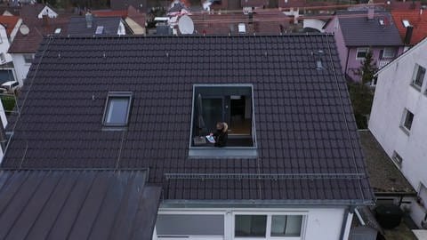 Zu sehen ist ein Hausdach von oben. Dort steht ein Mann auf dem Balkon und Blickt auf einen Plan. (Foto: SWR)