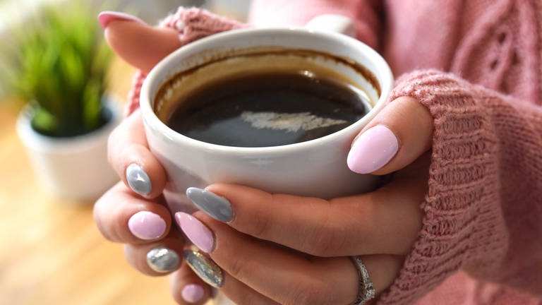 Wie gefährlich ist zu viel Kaffee? Frau hält eine Tasse Kaffee in der Hand.