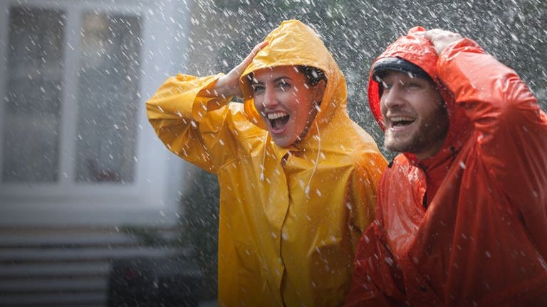 Zwei Personen stehen im Regen in einer gelben und roten Regenjacke. Sicher und trocken durch den Regen? (Foto: Adobe Stock, Sam Edwards / Caia Image)