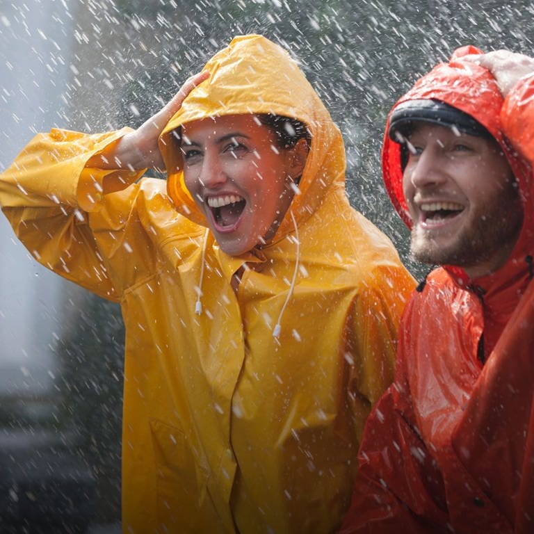 Zwei Personen stehen im Regen in einer gelben und roten Regenjacke. Sicher und trocken durch den Regen? (Foto: Adobe Stock, Sam Edwards / Caia Image)