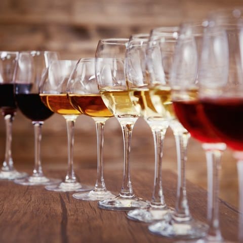 Mehrere Weingläser stehen in einer Reihe, gefüllt mit alkoholfreien Weinsorten: Weißwein, Rotwein und Rose.