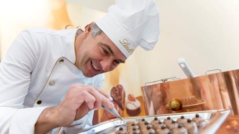 Ein Chocolatier mit Kochmütze von Lindt verziert Pralinen. Marktcheck checkt Lindt - wie gut ist die Schokolade?