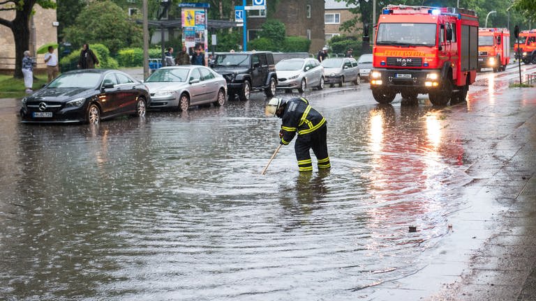 Eine Feuerwehrfrau steht auf einer von starkem Regen überfluteten Straße.