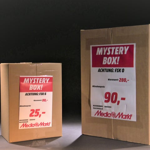 Zwei Mystery Boxen von MediaMarkt stehen nebeneinander. Auf den Kartons sind Warenwert und Kaufpreis angegeben.