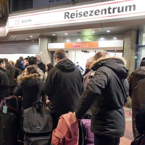 In einer Bahnhofshalle der deutschen Bahn stehen Menschen wegen Verspätungen der Züge vor dem Reisezentrum.