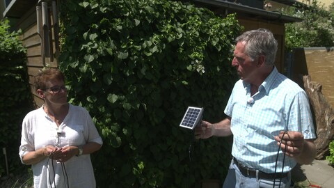 SWR Gartenexperte Werner Ollig zeigt Gartenliebhaberin Judith Marx ein Solarbewässerungssystem vor einer grün bewachsenen Wand eines Gartenhauses. (Foto: SWR)