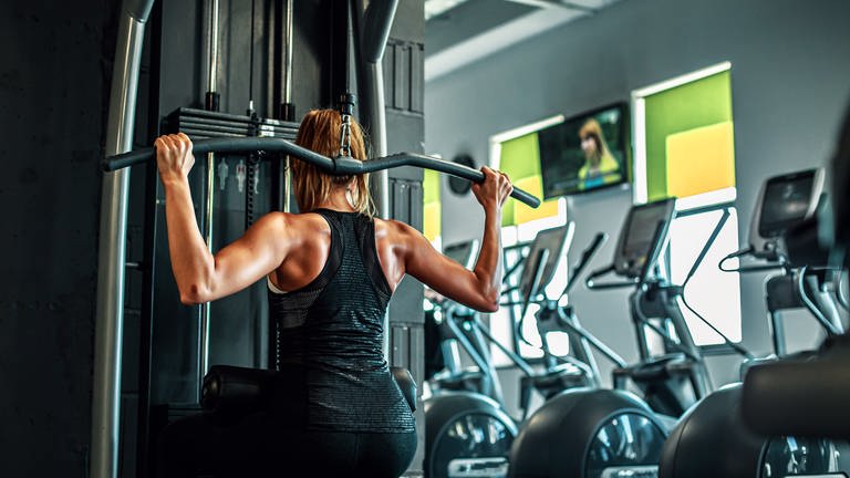 Eine Frau trainiert ihren Rücken in einem Fitnessstudio mit einer Latzugmaschine.
