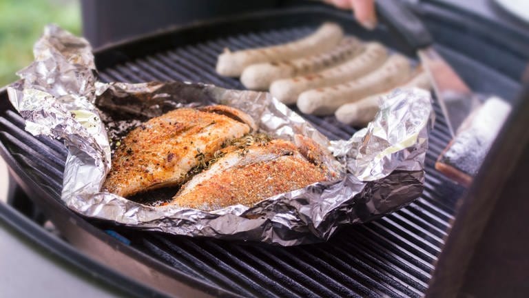 Fisch liegt in Alufolie auf einem Grill. Viele verwenden regelmäßig Alufolie, zum Beispiel zum Verpacken oder Abdecken von Essen und Lebensmitteln. Das ist nicht immer eine gute Idee - für die Gesundheit und die Umwelt.