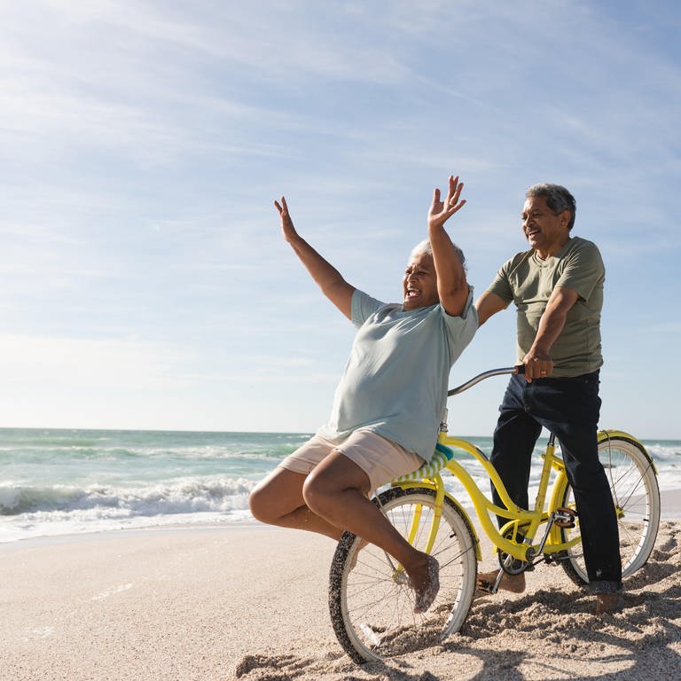 Senioren in Rente am Strand mit einem Fahrrade und sehr guter Laune.