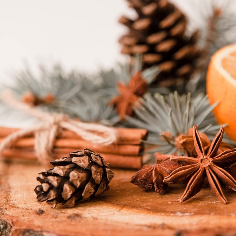 Weihnachtsgewürze, Tannenzapfen und Orangen auf hölzernem Hintergrund.
