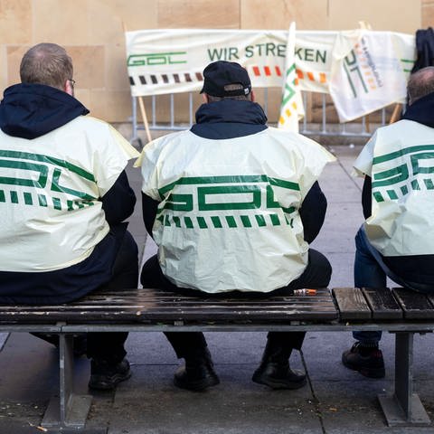Teilnehmer eines Warnstreiks der Gewerkschaft Deutscher Lokomotivführer (GDL) sitzen vor dem Hauptbahnhof auf einer Bank. (Foto: dpa Bildfunk, picture alliance/dpa | Marijan Murat)