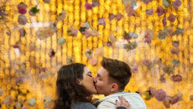 Ein junges Paar küsst sich vor einem Hintergrund von Goldmünzen