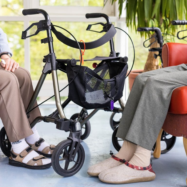 In einer Sitzgruppe in einem Pflegeheim sitzen zwei Senioren mit Rollatoren  (Foto: dpa Bildfunk, Picture Alliance)
