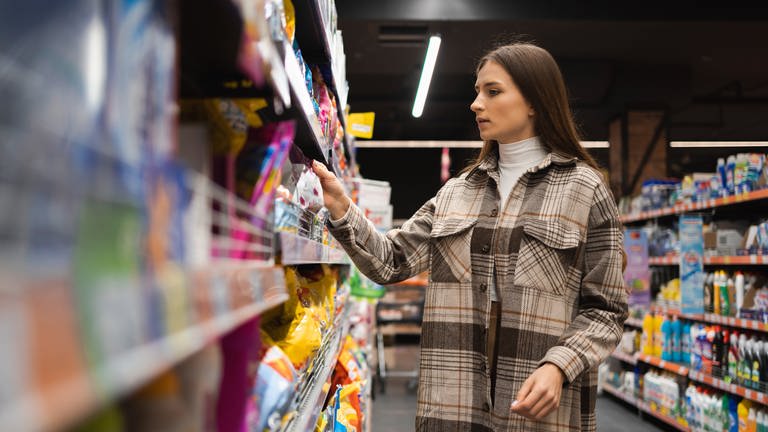 Eine Frau guckt sich Lebensmittel im Supermarkt an. Katjes, Oreo, Sanella – im Supermarkt entdecken wir immer wieder versteckte Preiserhöhungen. Die aktuellen Tricks der Hersteller.    (Foto: Adobe Stock)