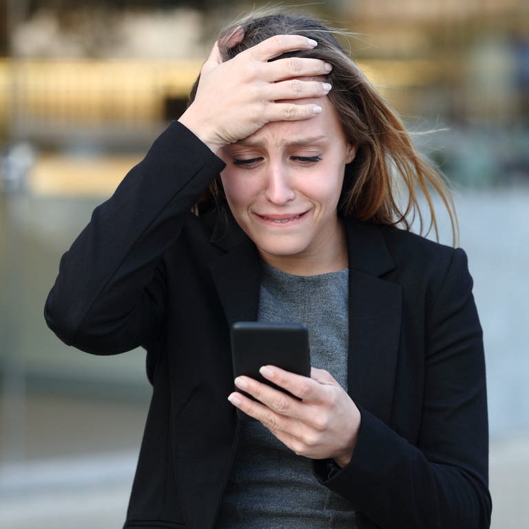 Eine Frau guckt aufgebracht auf ihr Handy, da sie Opfer von Sim Swapping geworden ist. Die Betrugsmasche kann nervenaufreibend und teuer werden! Wie Betrüger Handynummern stehlen und wie ihr euch gegen SIM Swapping schützen könnt. 