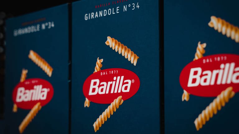 Blaue Nudelpackungen mit Rotem Barilla-Logo stehen in einem Regal.
