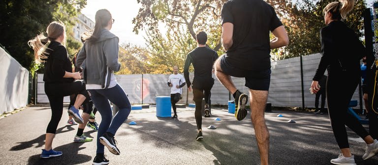 Eine Gruppe von Menschen treibt draußen Sport. Sie tragen Sportkleidung und laufen auf der Stelle. (Foto: Unsplash / Gabin Vallet)