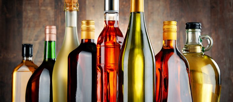 Glasflaschen verschiedene Sorten von Alkohol wie beispielsweise Sekt, Wein oder Rum stehen nebeneinander aufgereiht auf einem Tisch. (Foto: Adobe Stock, monticellllo)