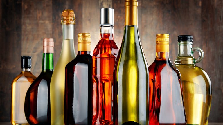 Glasflaschen verschiedene Sorten von Alkohol wie beispielsweise Sekt, Wein oder Rum stehen nebeneinander aufgereiht auf einem Tisch. (Foto: Adobe Stock, monticellllo)