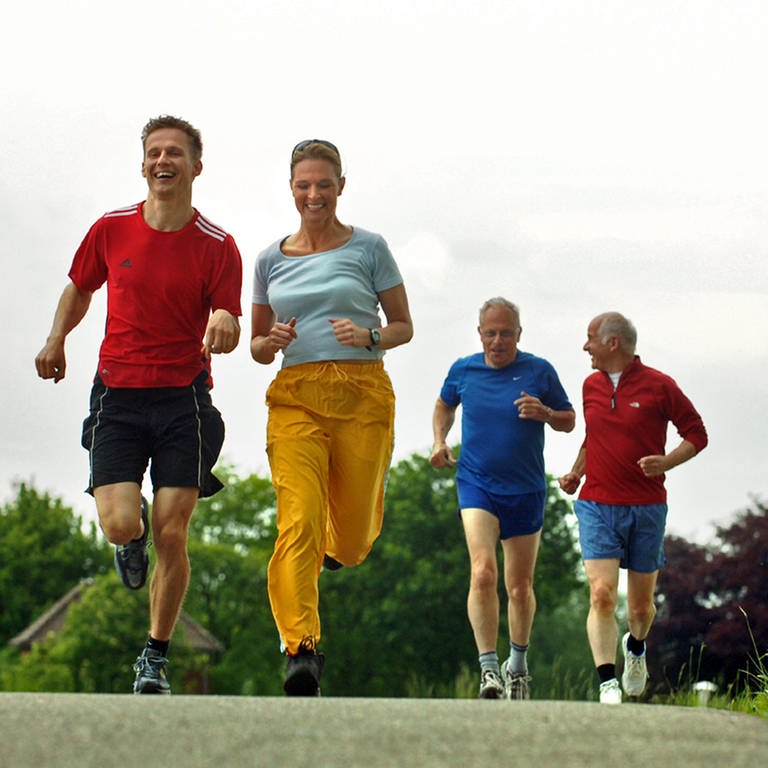 Drei Männer und eine Frau joggen gut gelaunt auf einer Landstraße. Sport kann vielen Krankheiten vorbeugen - sogar Krebs. (Foto: dpa Bildfunk, Picture Alliance)