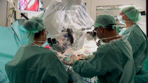Eine Person wird in einem OP-Saal am Gehirn operiert, um sie herum stehen zwei Ärzte. (Foto: SWR)