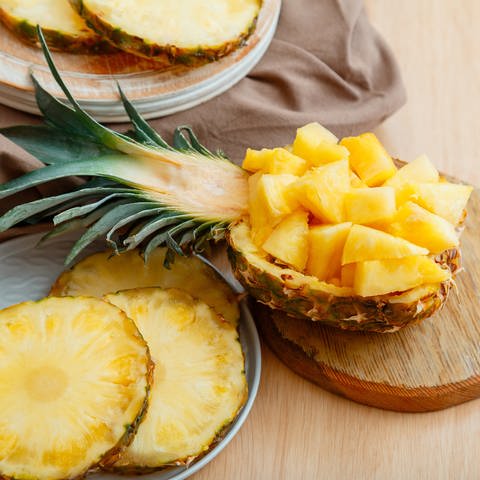 Geschnittene, gewürfelte Ananas in einer halbierten Ananas, daneben Ananas geschält und in Ringen (Foto: Adobe Stock, Beton Studio)