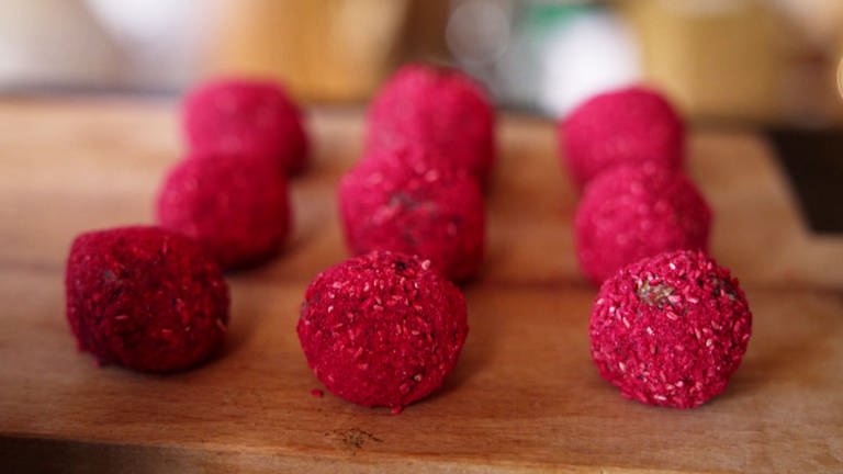 Rote Energy-Balls liegen auf einem Holzbrett. Müsliriegel in Rund: So kann man Energy Balls mit Haferflocken, Cranberrys und Himbeeren leicht selber machen. Ein Rezept. (Foto: SWR)