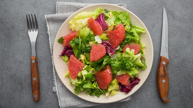 Grüner Salat mit Radicchio und Grapefruit-Stücken liegt appetitlich angerichtet auf einem Teller. Bitterstoffe sind gesund!