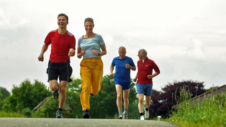 Drei Männer und eine Frau joggen gut gelaunt auf einer Landstraße. Sport kann vielen Krankheiten vorbeugen - sogar Krebs.