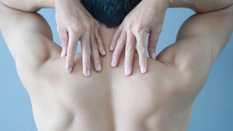 Eine Person von hinten, die mit den Händen zu ihren Schultern greift. Sollte bei Schulterschmerzen operiert werden oder lieber nicht? (Foto: Adobe Stock, AdobeStock/mraoraor)