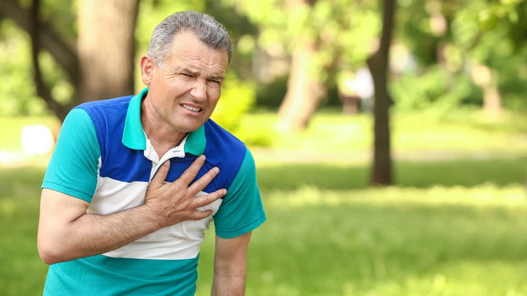 Ein älterer Mann greift sich mit schmerzverzerrtem Gesicht an den Brustkorb im Bereich des Herzens. (Foto: Adobe Stock)