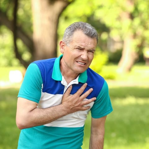Ein älterer Mann greift sich mit schmerzverzerrtem Gesicht an den Brustkorb im Bereich des Herzens.