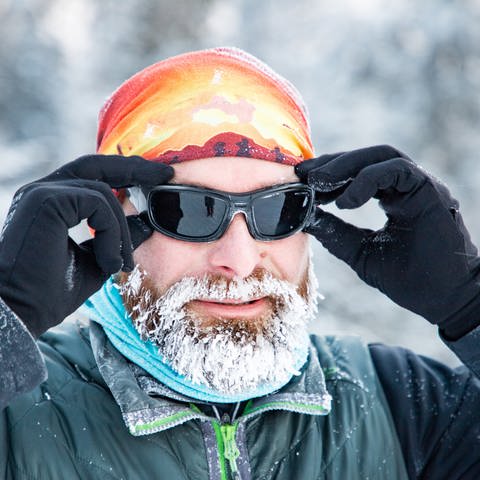 Mann mit Mütze, Handschuhen, Sonnenbrille und vereistem Bart. Ist Kälte gut oder schlecht für die Gesundheit?