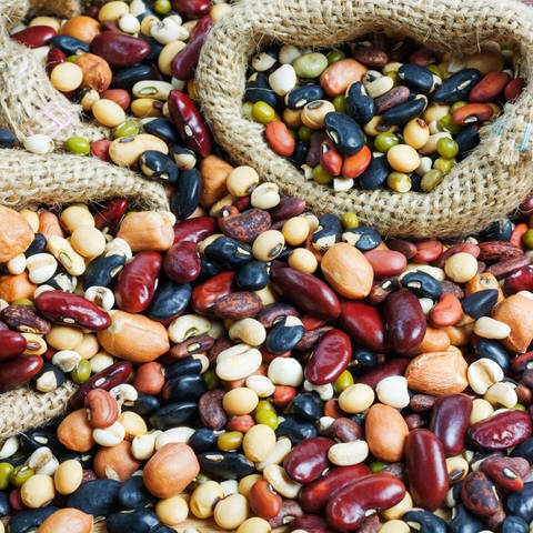 Verschiedene Hülsenfrüchte wie Bohnen, Kichererbsen, Linsen liegen auf einem Haufen. So gesund sind Hülsenfrüchte und das hilft gegen Blähungen.