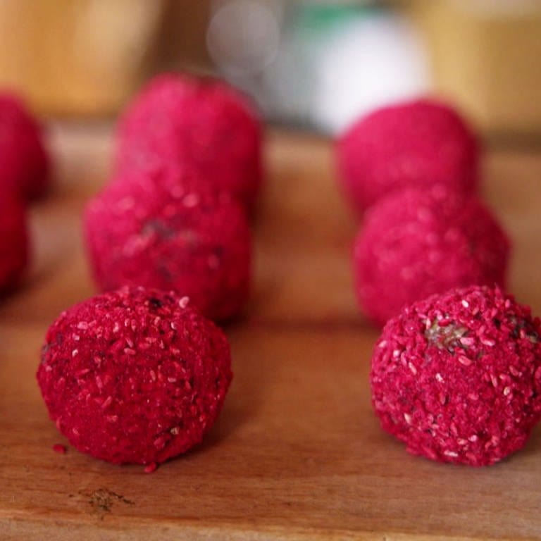 Rote Energy-Balls liegen auf einem Holzbrett. Müsliriegel in Rund: So kann man Energy Balls mit Haferflocken, Cranberrys und Himbeeren leicht selber machen. Ein Rezept. (Foto: SWR)