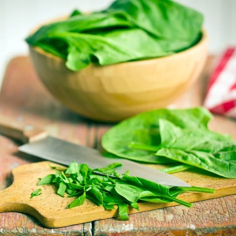 Spinat liegt geschnitten auf einem Brett. Spinat ist gesund und lecker. Mit welchen Rezepten schmeckt das Blattgemüse am besten? Und hilft Spinat möglicherweise beim Muskelaufbau? 