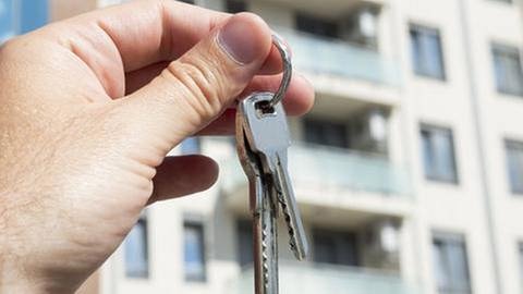 Eine Hand hält einen Wohnungschlüssel in die Höhe vor einer Hausfassade. (Foto: Getty Images, Thinkstock -)