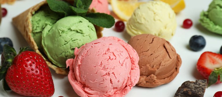 Verschiedene Eissorten liegen kugelweise mit frischem Obst auf einem weißen Untergrund. (Foto: Colourbox)