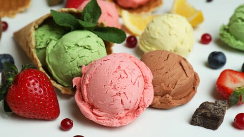 Verschiedene Eissorten liegen kugelweise mit frischem Obst auf einem weißen Untergrund. (Foto: Colourbox)
