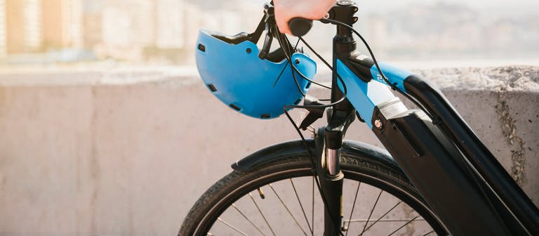 Ein Mann fährt ein E-Bike. Am Lenker hängt ein blauer Helm. (Foto: Colourbox, COLOURBOX52454195)