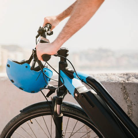 Ein Mann fährt ein E-Bike. Am Lenker hängt ein blauer Helm. (Foto: Colourbox, COLOURBOX52454195)