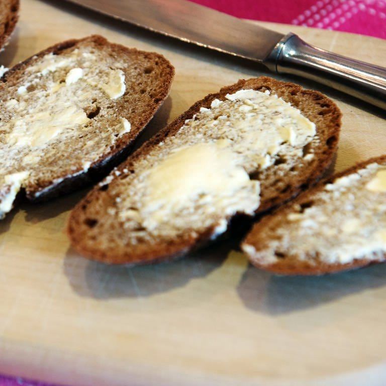 Vier Scheiben Brot liegen mit Butter bestrichen auf einem Brettchen auf dem Tisch. Welche Butter ist am besten? (Foto: dpa Bildfunk, Picture Alliance | Arno Burgi)