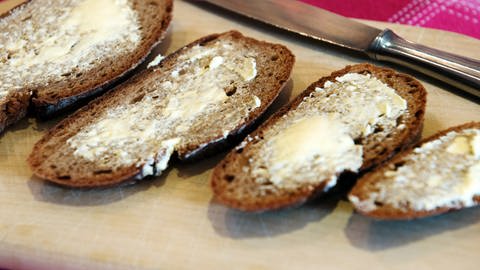 Vier Scheiben Brot liegen mit Butter bestrichen auf einem Brettchen auf dem Tisch. Welche Butter ist am besten? (Foto: dpa Bildfunk, Picture Alliance | Arno Burgi)