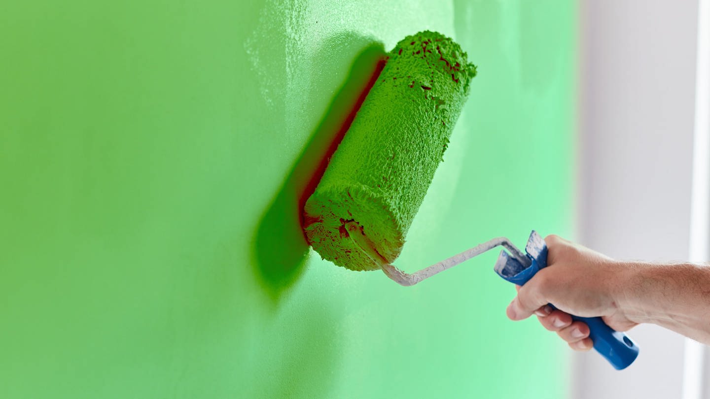 Person streicht mit Farbrolle eine Wand in einem hellgrünen Farbton. (Foto: Adobe Stock / Artur Nyk (390824219))