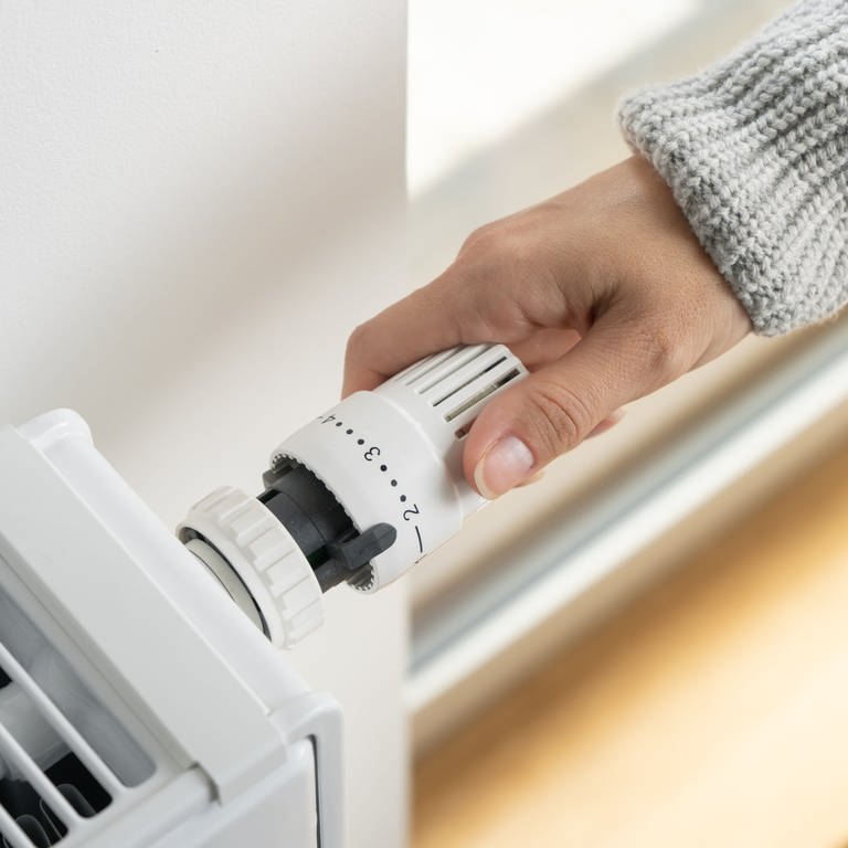 Eine Person mit grauem Pulli greift von rechts das Thermostat einer Heizung, die auf Stufe 2 gestellt ist. (Foto: Colourbox)