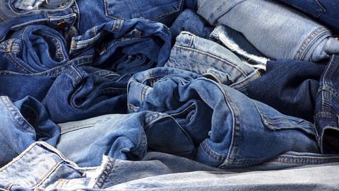 Die Nahaufnahme zeigt einen Haufen Jeans in verschiedenen blau Tönen. Nachhaltige Mode: so geht Jeans ohne Chemie in der Herstellung. (Foto: Adobe Stock)